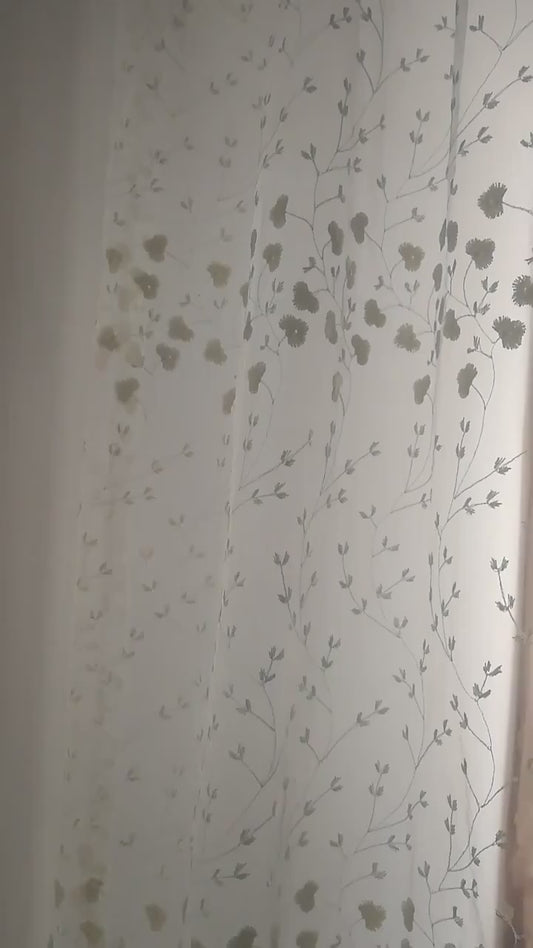 Zoom sur un voilage blanc cassé à fleurs brodées illuminé par la lumière naturelle.