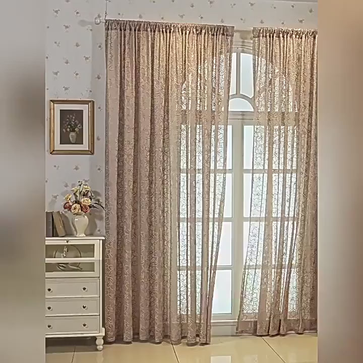 Vue d’ensemble d’un grand rideau translucide à fleurs installé sur une fenêtre cintrée, dans un intérieur classique avec commode et déco florale.