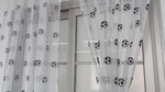 Voilages blancs ornés de motifs de ballons de football, suspendus à une tringle au-dessus d’une grande fenêtre moderne.