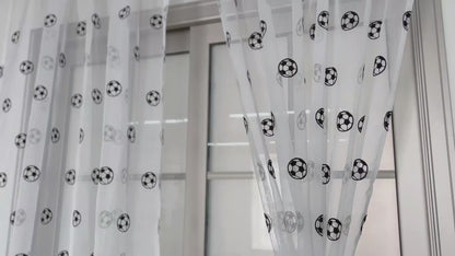 Voilages blancs ornés de motifs de ballons de football, suspendus à une tringle au-dessus d’une grande fenêtre moderne.