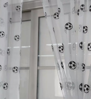 Voilages blancs ornés de motifs de ballons de football, suspendus à une tringle au-dessus d’une grande fenêtre moderne.