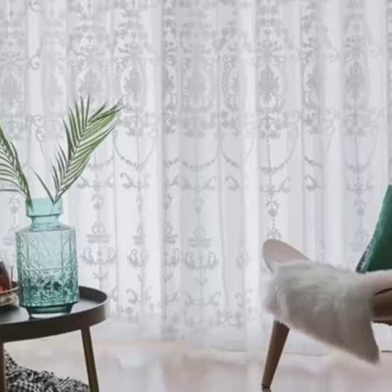 Vue d'ensemble d'un salon avec des rideaux blancs brodés, mettant en valeur la lumière naturelle et la décoration moderne.