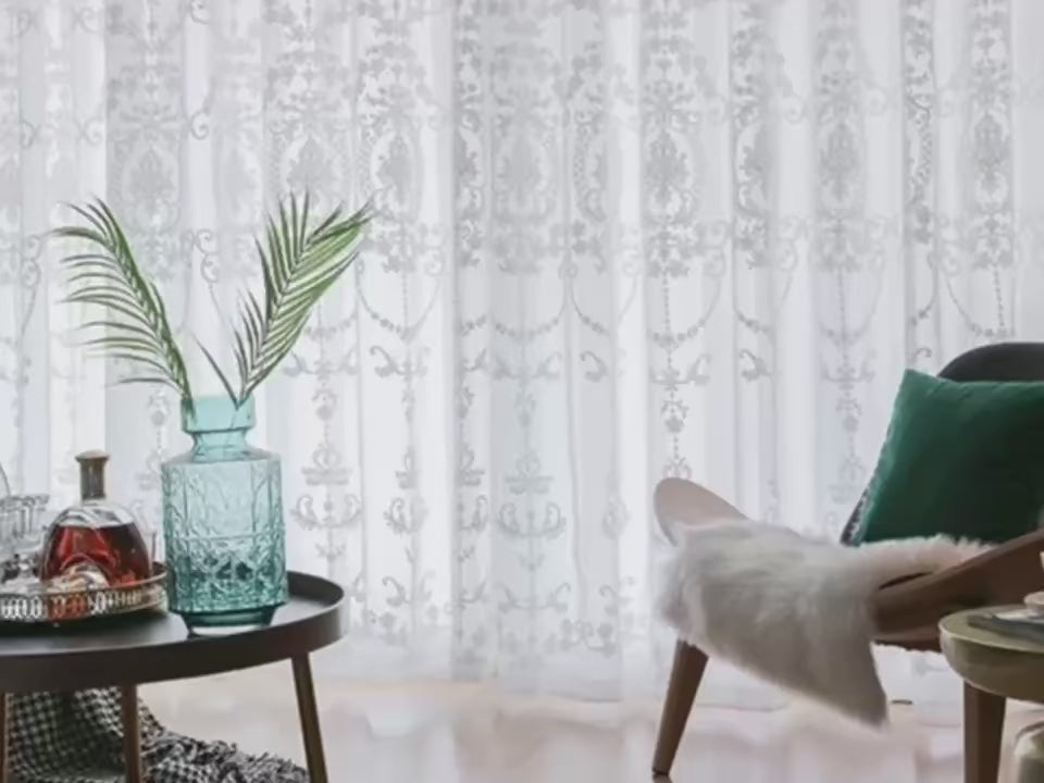 Vue d'ensemble d'un salon avec des rideaux blancs brodés, mettant en valeur la lumière naturelle et la décoration moderne.