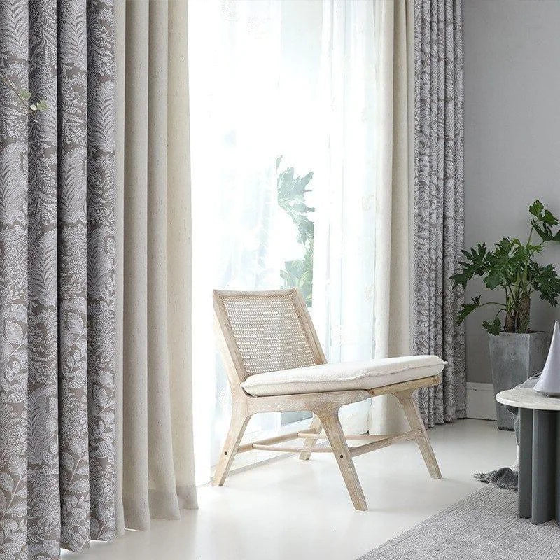 Coin détente élégant avec chaise bois clair, rideaux américains à motifs et rideaux unis, sur fond de lumière naturelle abondante.