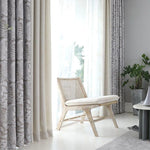 Coin détente élégant avec chaise bois clair, rideaux américains à motifs et rideaux unis, sur fond de lumière naturelle abondante.