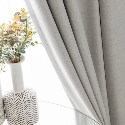 Rideau élégant de couleur grise, idéal pour sublimer votre décoration d'intérieur moderne. Parfait pour ajouter une touche de sophistication à votre salon ou chambre à coucher. Accompagné d'un vase décoratif avec des plantes artificielles pour un style raffiné et contemporain.