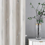 Rideau décoratif moderne avec motif ondulé argenté, idéal pour un salon élégant. Le rideau est présenté à côté d'un vase cylindrique transparent avec des branches de feuillage, ajoutant une touche zen et naturelle à l'intérieur. Parfait pour créer une atmosphère apaisante et sophistiquée dans votre espace de vie.