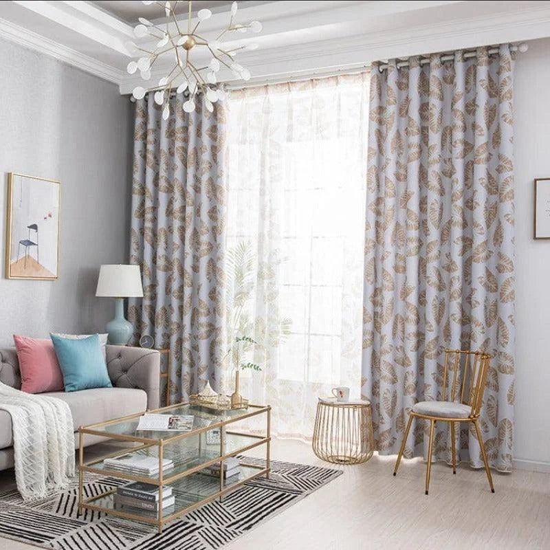 Salon moderne avec rideaux à motif de feuilles dans des tons neutres, canapé confortable avec coussins colorés, table basse en verre élégante et lampe sur pied, ambiance lumineuse et décor raffinée idéale pour une décoration intérieure contemporaine.