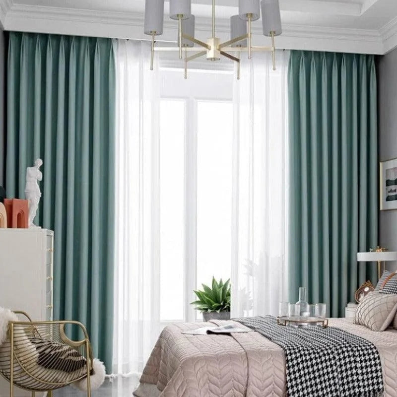 Chambre moderne avec rideaux vert émeraude et voilages blancs, offrant une ambiance élégante et apaisante. Le design du luminaire et les décorations contemporaines complètent la décoration raffinée de la pièce. Cette chambre bien aménagée crée un espace confortable et accueillant.