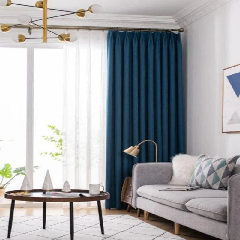 Rideaux bleus élégants habillant un salon moderne avec canapé gris, table basse design et décoration murale artistique, idéal pour une ambiance chaleureuse et contemporaine.