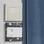 Décor moderne avec échantillons de différentes textures et couleurs. Bloc blanc nuancé, élément transparent à rayures verticales, et panneau noir moucheté de blanc. Rideau bleu à droite, ajoutant une touche élégante à l'ensemble. Idéal pour l'inspiration design intérieur et choix de matériaux.