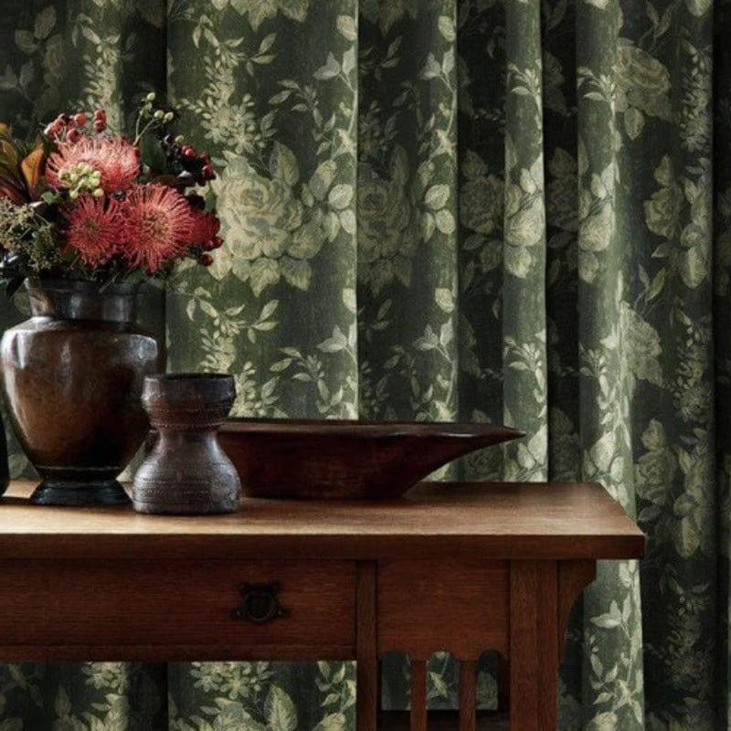 Rideau à motifs floraux verts offrant une ambiance naturelle et apaisante, idéal pour un salon élégant. En arrière-plan, tableau en bois surmonté de vases décoratifs et fleurs colorées ajoutant une touche d'élégance rustique.