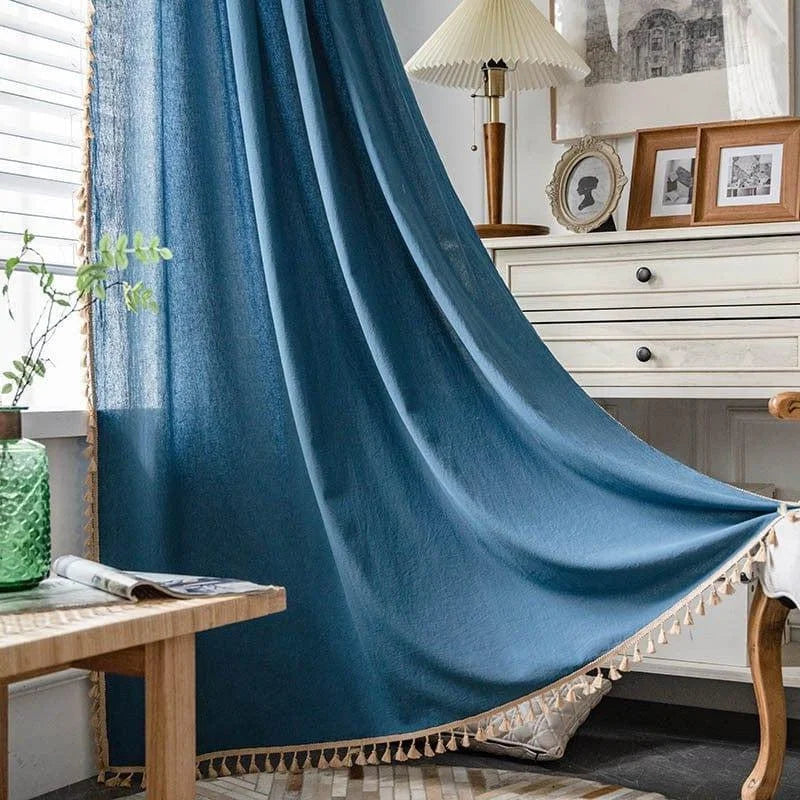 Rideau bleu élégant avec franges décoratives, embellissant une pièce lumineuse avec des meubles en bois clair. Parfait pour ajouter une touche sophistiquée à votre intérieur tout en permettant une douce lumière naturelle de filtrer. Idéal pour le salon ou la chambre à coucher. Décoration harmonieuse et chic.