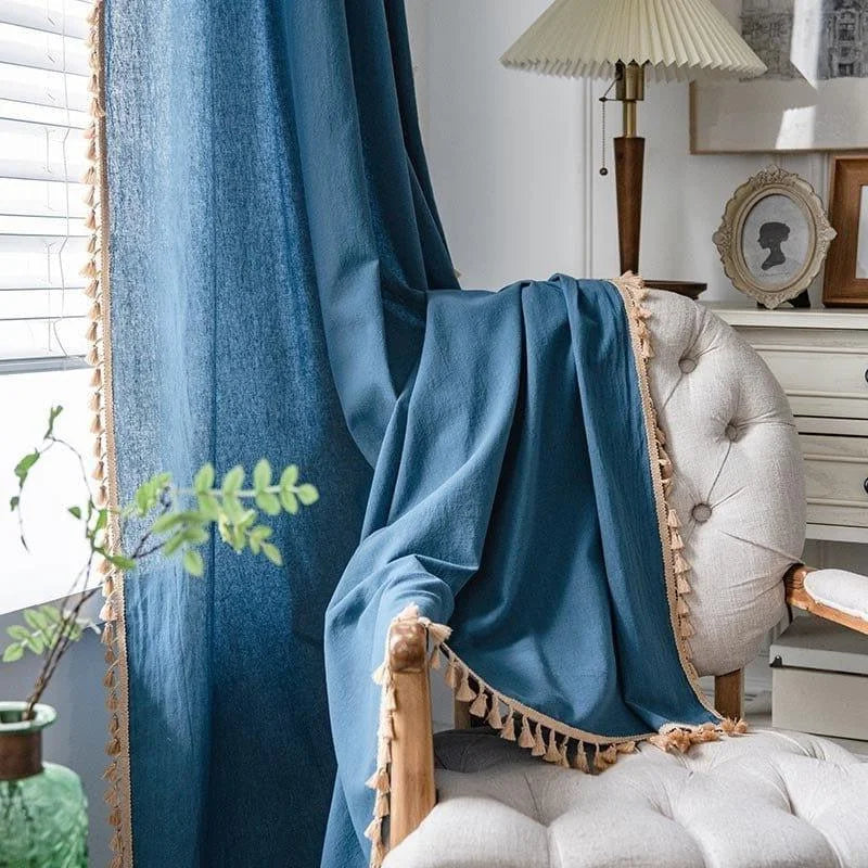 Voilage élégant bleu avec bordure à pompons beige, décorant un fauteuil dans un salon lumineux et moderne. Parfait pour ajouter une touche de sophistication à votre intérieur.
