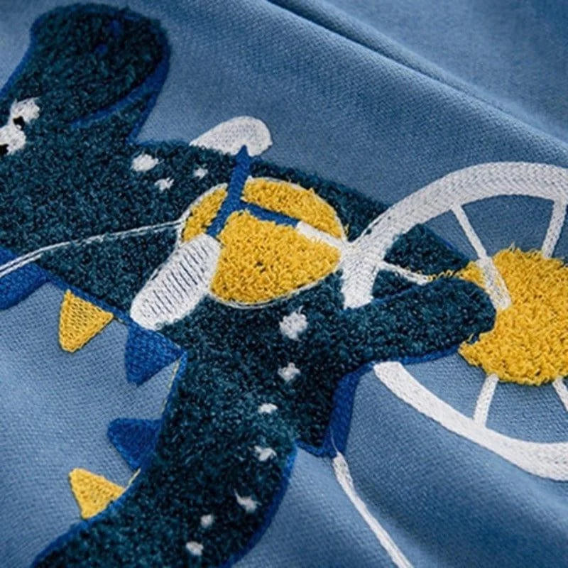 Image d'un motif brodé représentant un dinosaure ludique et coloré sur fond bleu. Ce design original ajoute une touche unique et amusante à n'importe quel vêtement pour enfants, parfait pour apporter de la joie et du style.