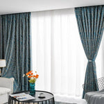 Rideaux élégants de couleur bleue avec motifs décoratifs suspendus dans un salon moderne lumineux. Intérieur sophistiqué avec table basse noire, vase décoratif, et canapés confortables. Accessoirisation florale ajoutant une touche de couleur vive. Parfait pour embellir votre espace de vie en offrant confort et style.