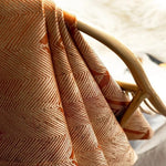 Plaid décoratif aux motifs géométriques orange et blanc suspendu sur un meuble en bois. Accessoire tendance pour embellir un salon ou une chambre, parfait pour ajouter une touche de sophistication et de chaleur à votre intérieur. Idée de décoration cosy et moderne.