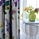 Rideau floral coloré suspendu devant une fenêtre, ajoutant une touche de fraîcheur printanière à la décoration intérieure. Le motif floral vibrant avec des nuances de violet, vert et bleu crée une ambiance accueillante et lumineuse. Parfait pour égayer un salon ou une chambre avec style et élégance. Idéal pour les espaces nécessitant un relooking avec une note naturelle et sophistiquée.