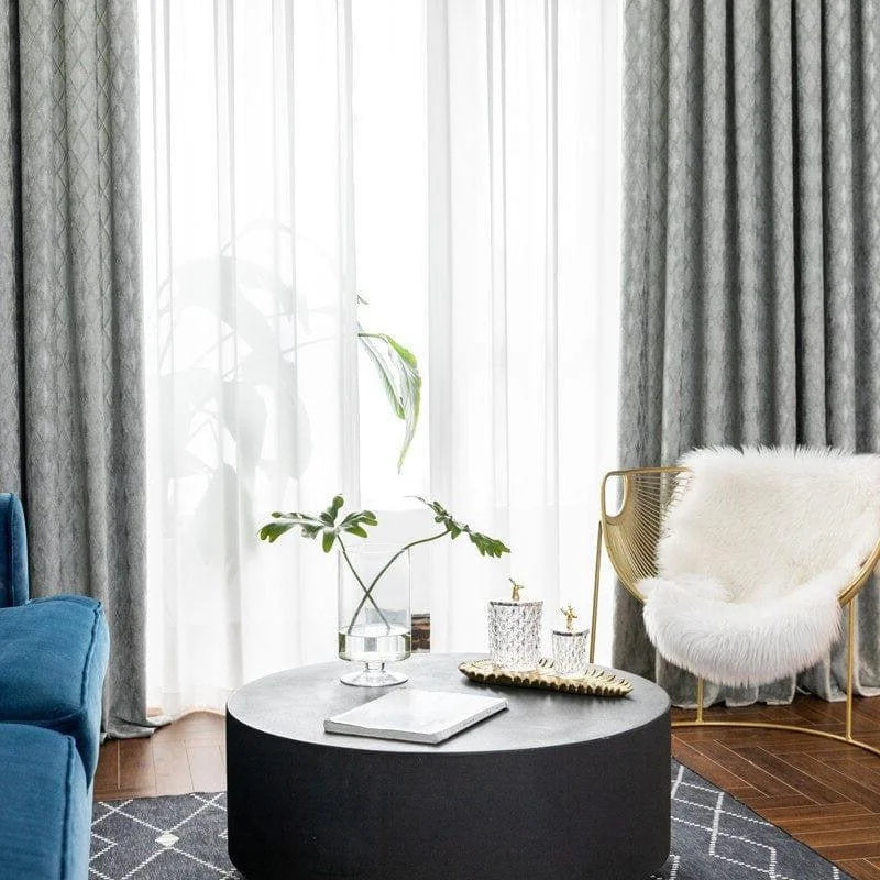 Salon moderne avec un fauteuil design doré et coussin confortable, décoration élégante avec table basse ronde noire, rideaux gris associés à un canapé bleu pour un espace de détente contemporain. Atmosphère lumineuse et accueillante.