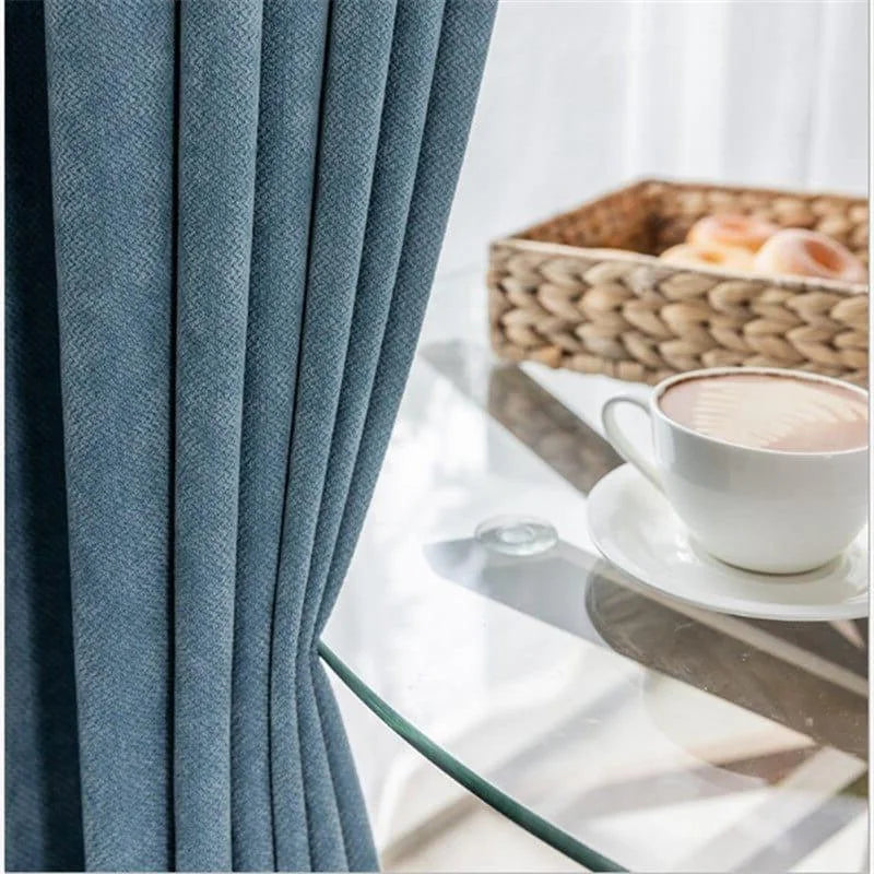 Rideaux opaques bleus pour salon moderne, ajoutant une touche élégante à votre décoration intérieure, accompagnés d'une table en verre minimaliste avec une tasse de café mousseux et un plateau tressé en arrière-plan.