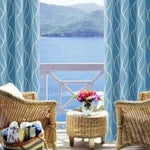 Paire de rideaux bleus à motifs ondulés, encadrant une vue panoramique sur la mer et les montagnes. Ambiance sereine avec fauteuils en osier et table basse décorée de fleurs colorées, parfaite pour un salon avec vue. Rideaux idéaux pour ajouter une touche élégante et relaxante à votre intérieur.