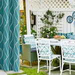 Espace extérieur élégant avec mobilier de jardin et décorations florales. La table blanche est accompagnée de chaises aux motifs modernes, parfaite pour des repas en plein air. Les coussins et rideaux en bleu ajoutent une touche de fraîcheur. Idéal pour aménager un coin détente sur votre terrasse ou patio.
