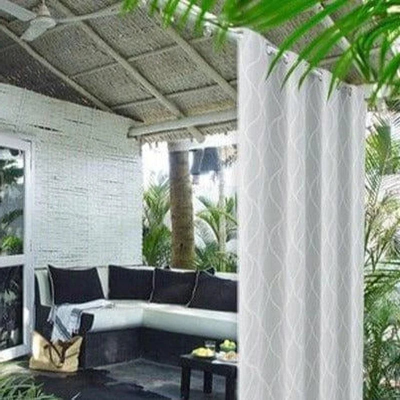 Rideau blanc élégant utilisé pour séparer un espace extérieur sous une pergola, apportant une touche moderne et sophistiquée à votre terrasse. Idéal pour créer une ambiance accueillante et privée, ce rideau est parfait pour les moments de détente en plein air, entouré de verdure tropicale.