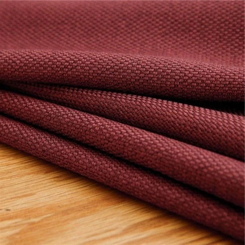 Texte alternatif: "Gros plan sur un rideau en tissu texturé de couleur bordeaux posé sur une surface en bois, mettant en valeur la qualité et la richesse de la matière pour une décoration intérieure élégante."