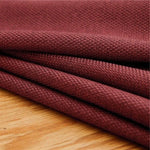 Texte alternatif: "Gros plan sur un rideau en tissu texturé de couleur bordeaux posé sur une surface en bois, mettant en valeur la qualité et la richesse de la matière pour une décoration intérieure élégante."