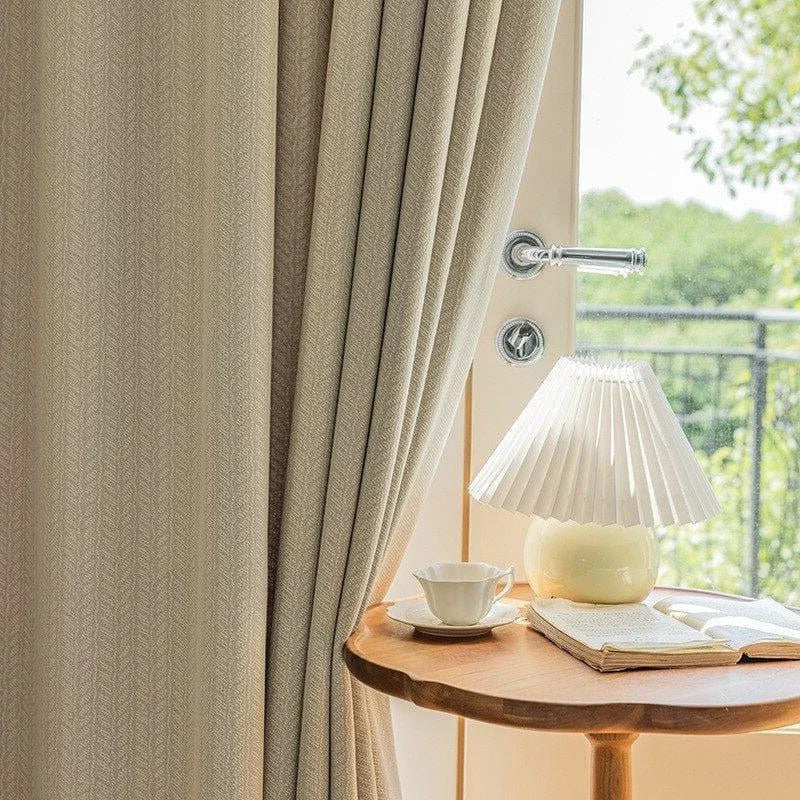 Rideau beige élégant suspendu à une fenêtre lumineuse, offrant une vue sur la nature environnante, accompagné d'une lampe design posée sur une table en bois, créant une ambiance chaleureuse et accueillante. Découvrez comment transformer votre intérieur avec style et luminosité.