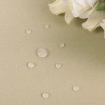 Image montrant un tissu beige avec des gouttes d'eau, illustrant ses propriétés déperlantes. Des fleurs blanches sont visibles dans le coin supérieur droit, ajoutant une touche élégante et raffinée à la présentation du produit. Cette image met en avant la résistance du tissu à l'eau, idéale pour des intérieurs contemporains.