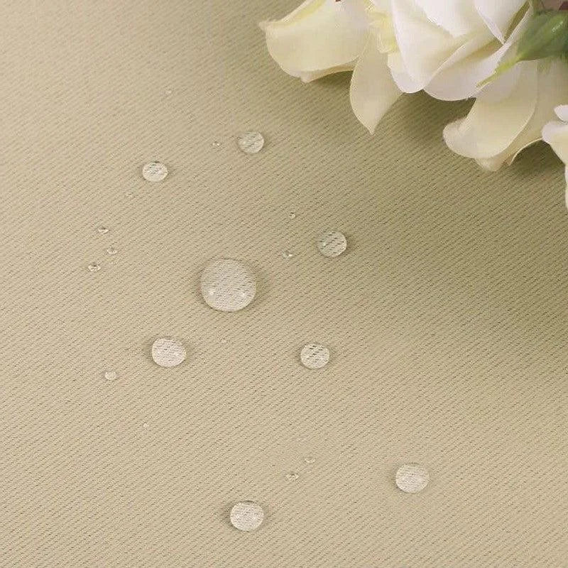 Image montrant un tissu beige avec des gouttes d'eau, illustrant ses propriétés déperlantes. Des fleurs blanches sont visibles dans le coin supérieur droit, ajoutant une touche élégante et raffinée à la présentation du produit. Cette image met en avant la résistance du tissu à l'eau, idéale pour des intérieurs contemporains.