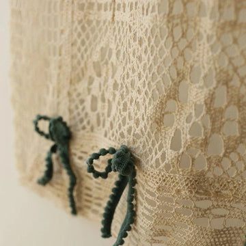 Image de gros plan d'un textile beige ajouré avec des motifs complexes, décoré de petits nœuds verts pour une touche élégante et raffinée, idéale pour les projets de design intérieur ou la confection de vêtements sophistiqués.