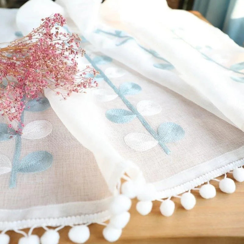 Voile décoratif avec motifs floraux bleus et détails pompons blancs, idéal pour ajouter une touche élégante et raffinée à votre intérieur. Parfait pour l'embellissement des fenêtres ou pour créer une ambiance légère et aérée dans votre espace de vie.