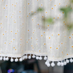 Rideau décoratif élégant avec motif de petites fleurs blanches et jaunes, accentué par une bordure ornée de pompons. Idéal pour ajouter une touche printanière à votre intérieur.