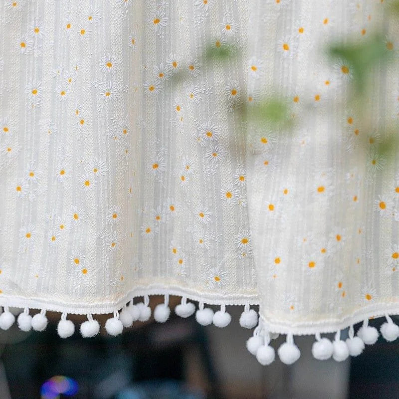 Rideau décoratif élégant avec motif de petites fleurs blanches et jaunes, accentué par une bordure ornée de pompons. Idéal pour ajouter une touche printanière à votre intérieur.