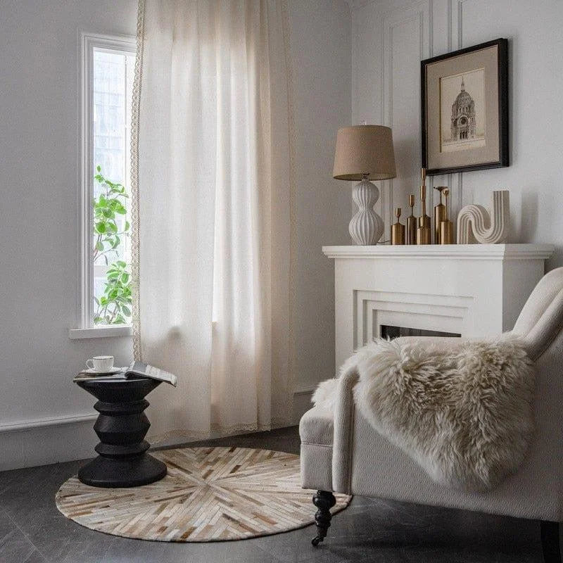 Salon élégant avec fauteuil blanc confortable et table d'appoint noire, décor moderne comprenant une lampe et des objets décoratifs dorés sur une cheminée blanche, atmosphère lumineuse avec rideaux transparents et lumière naturelle.