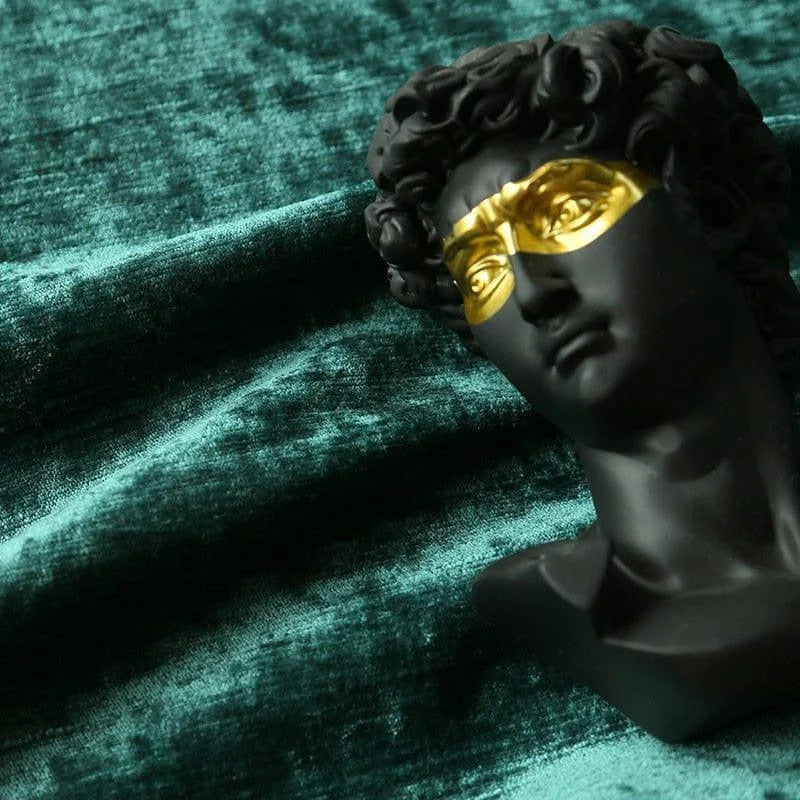 Buste décoratif noir avec masque doré, posé sur un fond texturé vert. Accessoire d'art unique pour la décoration intérieure, ajoutant une touche moderne et élégante à tout espace de vie. Idéal pour les amateurs de design contemporain cherchant à enrichir leur environnement avec une pièce originale et artistique.