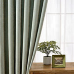 Rideau vert au motif chevron, apportant une touche élégante et moderne à votre intérieur. Idéal pour filtrer la lumière tout en ajoutant du style à votre salon ou chambre. Complément parfait d'une décoration contemporaine, avec un joli contraste sur une table en bois ornée d'une plante en pot.