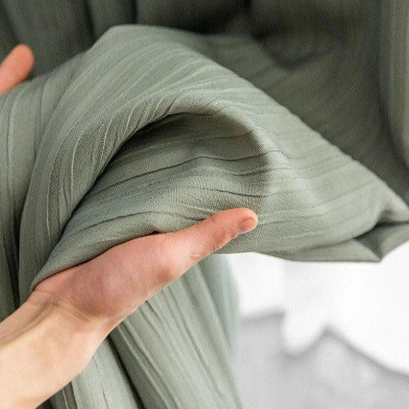 Textile plié gris tenu à la main, illustration de tissu pour ameublement intérieur, texture plissée, zoom sur les détails du tissu, style moderne et élégant, ambiance minimaliste et douce.