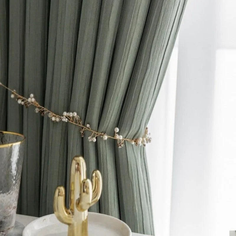 Rideau élégant vert clair, attaché par un cordon décoratif orné de perles blanches, ajoutant une touche sophistiquée et moderne à la décoration intérieure. Accessoires dorés en avant-plan, mettant en valeur le design luxueux pour un salon ou une chambre à coucher. Style contemporain et raffiné adapté à tous les environnements de maison.
