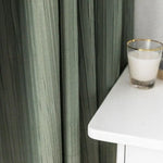 Rideaux verts élégants tombant harmonieusement à côté d'une table blanche moderne avec un verre vide, apportant une touche de sophistication à la décoration intérieure.