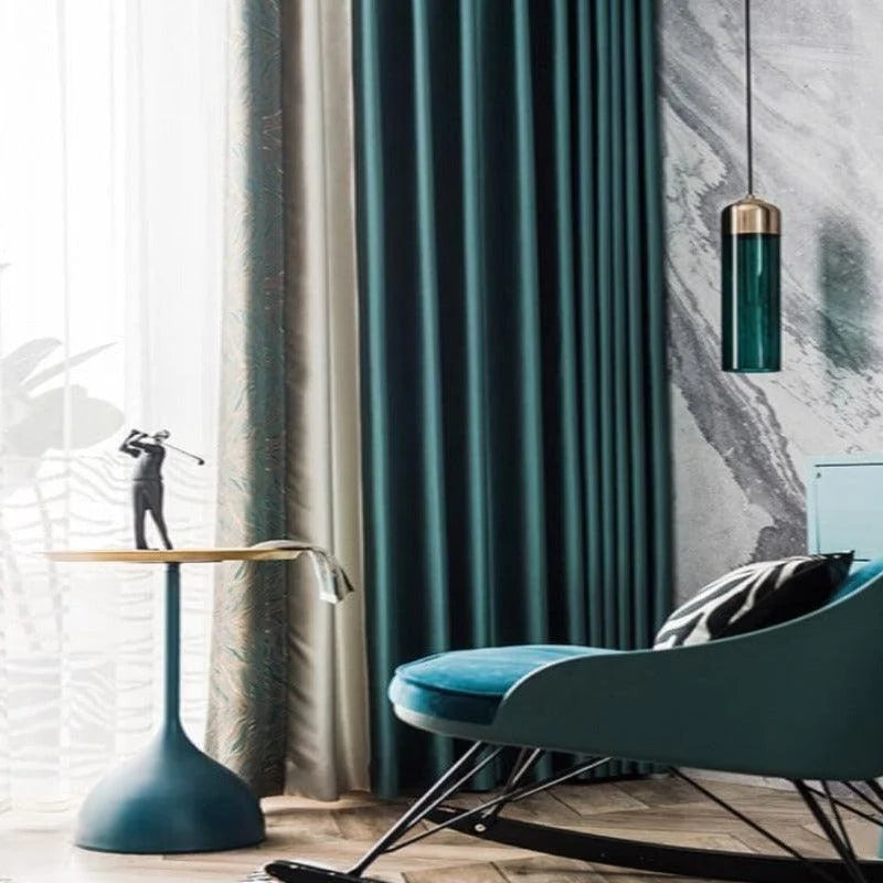 Fauteuil à bascule moderne bleu dans un salon élégant, associé à un rideau en dégradé de couleurs, une table d'appoint minimaliste avec une figurine décorative, et un luminaire suspendu contemporain. Ambiance chic et design élégant pour un intérieur raffiné.