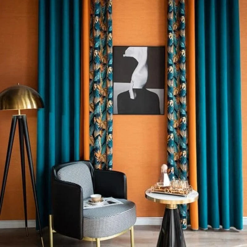 Salle de séjour élégante avec rideaux bleus et imprimés tropicaux, accentuant un mur orange moderne. Lampe sur trépied dorée apportant une touche lumineuse, et fauteuil noir à motif géométrique complétant l'espace. Table d'appoint avec déco sophistiquée, idéale pour les espaces contemporains.