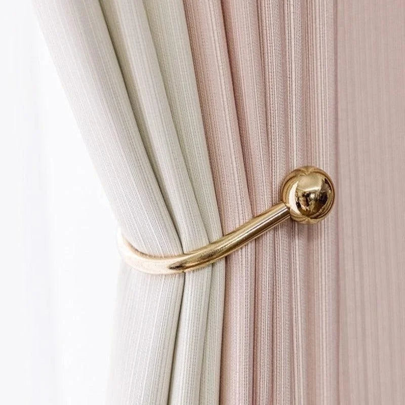 Attache-rideaux dorée élégante retenant des rideaux bicolores, ajoutant une touche de luxe et de sophistication à votre décoration intérieure. Accessoire pratique et esthétique pour un aménagement raffiné.