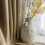 Vase décoratif blanc au design moderne, placé devant un rideau élégant beige avec motif de feuilles, apportant une touche naturelle et chic à votre intérieur. Idéal pour embellir votre salon ou chambre.