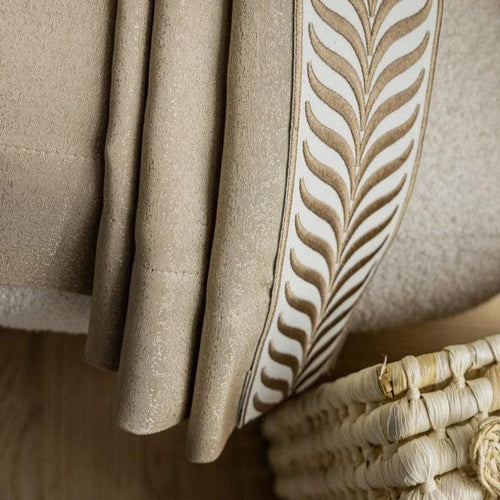 Plaid beige élégant avec motif décoratif, posé sur un fauteuil confortable. Accessoire idéal pour salon moderne, apportant chaleur et style à votre décoration intérieure. Parfait pour les soirées cocooning.