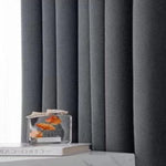 Rideaux opaques gris modernes dans un intérieur minimaliste, ajoutant une touche d'élégance. Parfait pour une décoration de salon ou de chambre à coucher. Complétés par un élément décoratif en verre sur une surface blanche pour un style raffiné.