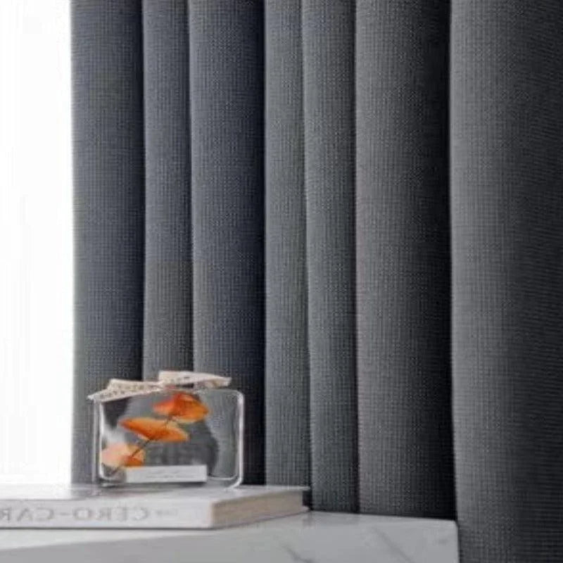 Rideaux opaques gris modernes dans un intérieur minimaliste, ajoutant une touche d'élégance. Parfait pour une décoration de salon ou de chambre à coucher. Complétés par un élément décoratif en verre sur une surface blanche pour un style raffiné.