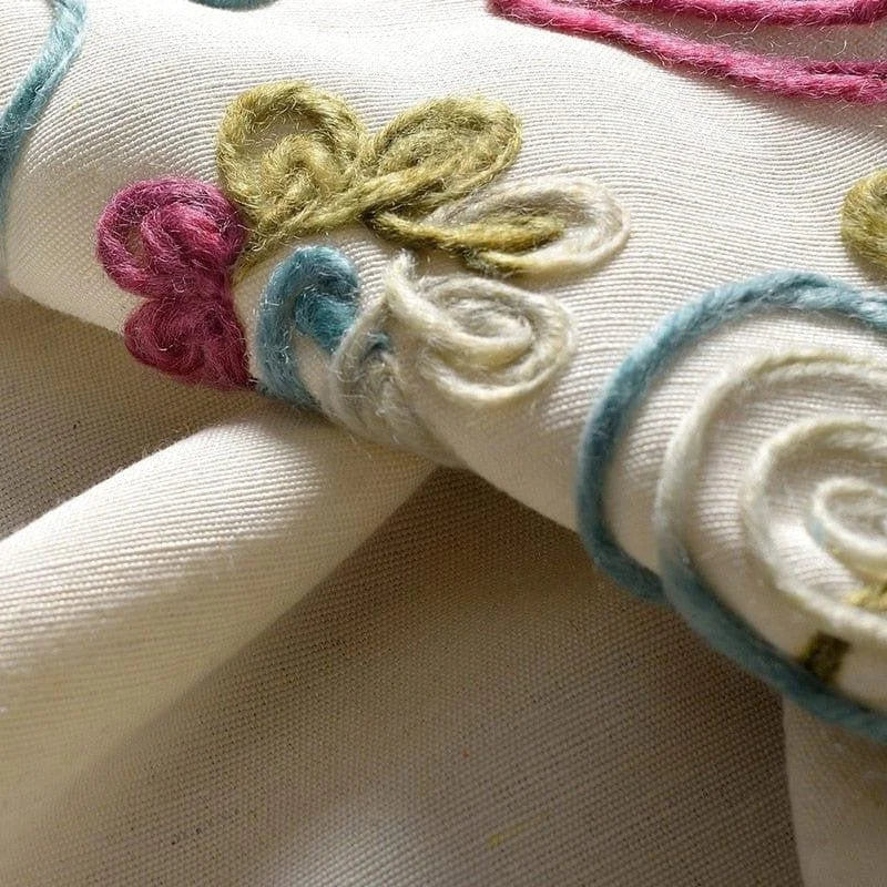 Gros plan d'un tissu délicatement orné de motifs floraux brodés en relief. Les motifs, aux teintes pastel de rose, vert et bleu, apportent une touche élégante et artistique, idéale pour embellir tout type d'intérieur. Cette décoration textile, alliant subtilité et originalité, s'adapte parfaitement aux tendances actuelles de la décoration d'intérieur.